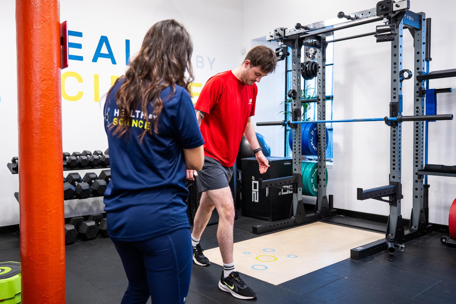 KA3_3304 A personal trainer conducting a movement assessment with a male client in a gym setting.