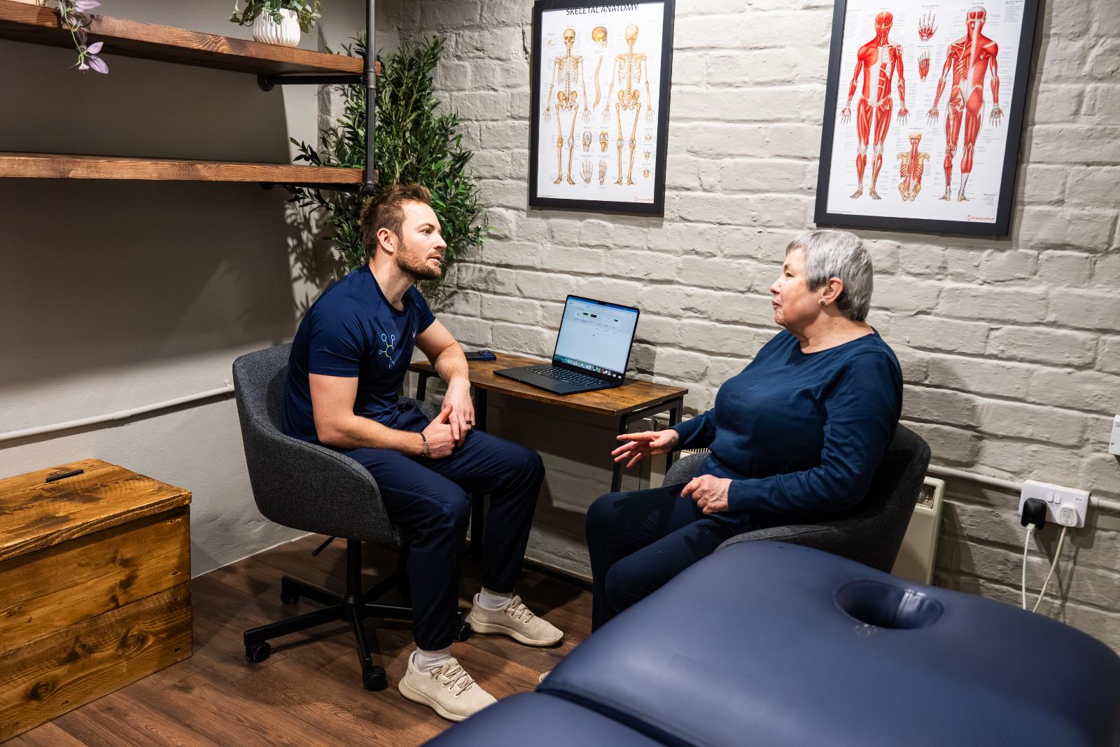 KA3_4217 A male physiotherapist in blue scrubs conducting an initial consultation with a patient in a private clinic room.