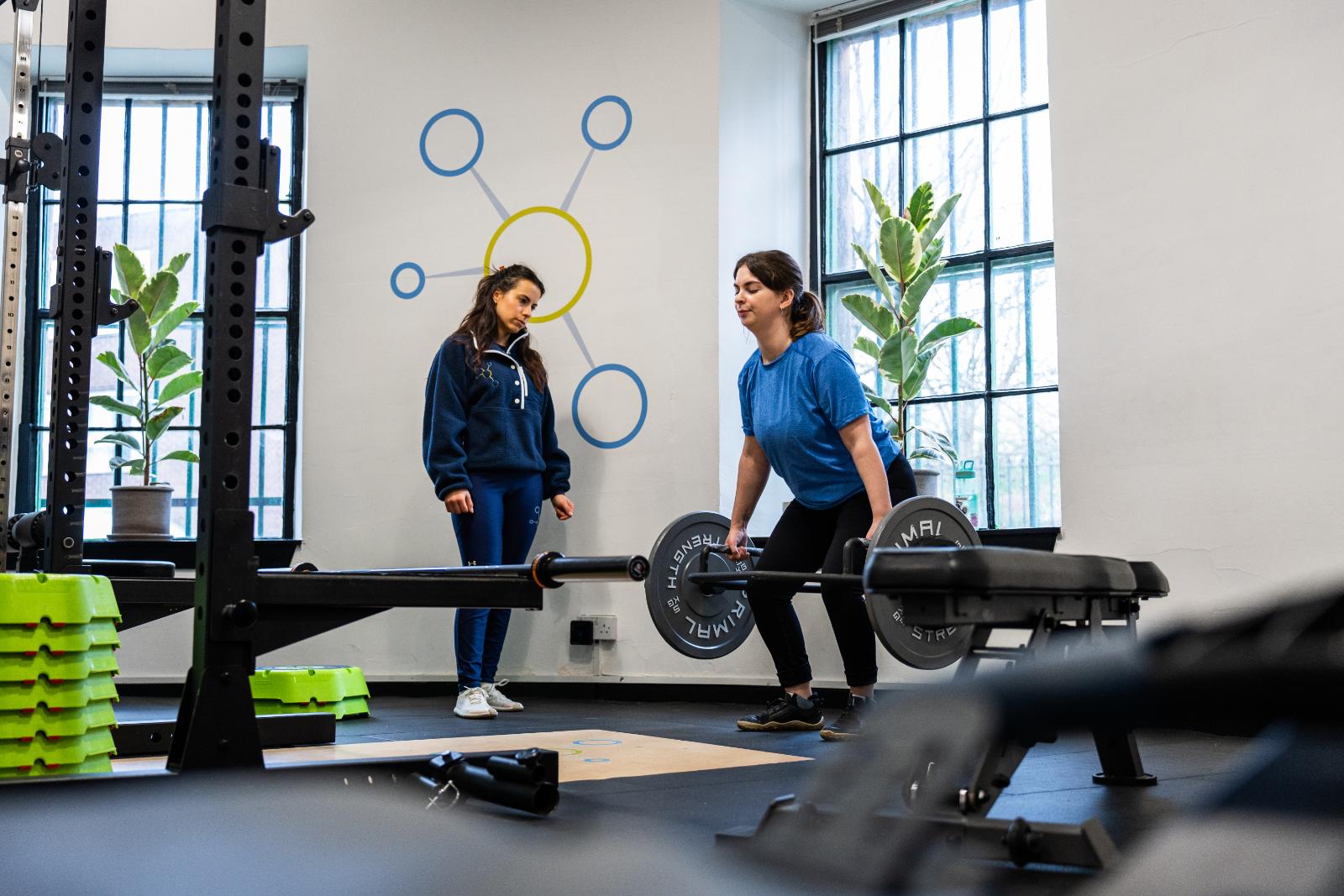 KA3_4432 A female personal trainer edinburgh coaching a woman during a barbell deadlift in a bright, modern gym in Leith.